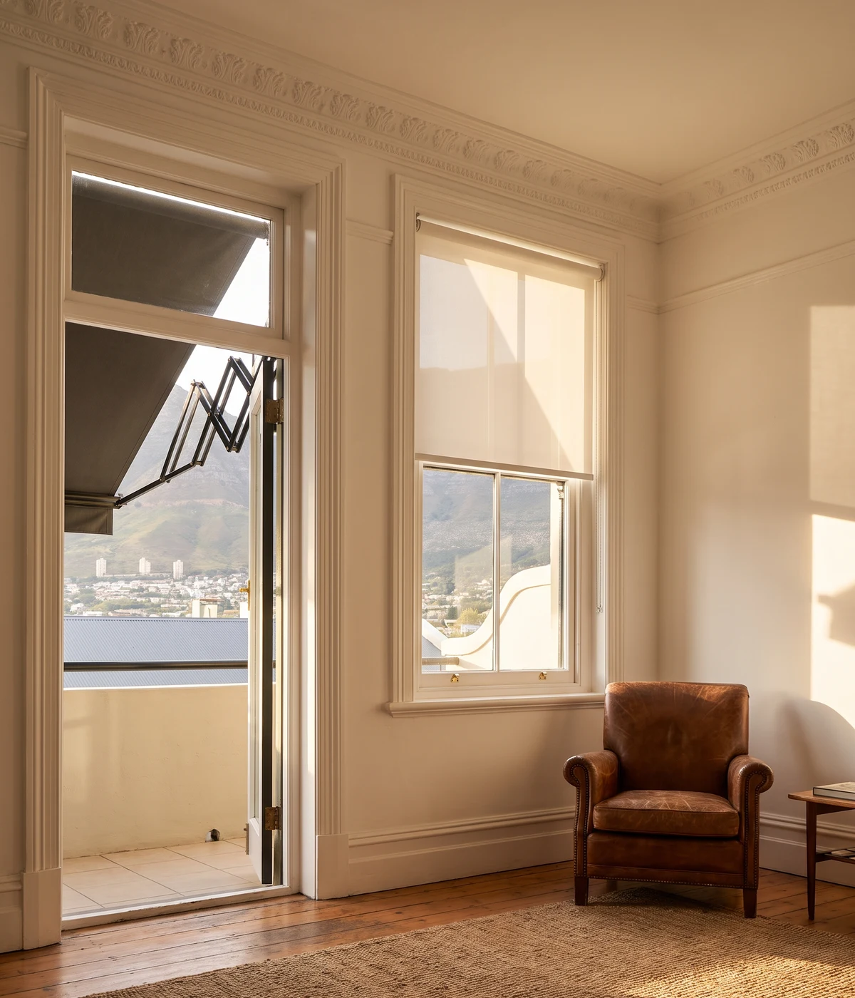 Living room in a Tamboerskloof heritage home with a sunscreen roller blind on the sash window and a fold-arm awning open over the balcony, Table Mountain slope views